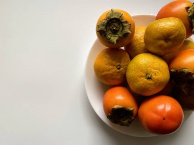 Doğal ışıkta beyaz bir tabakta sergilenen canlı bir meyve çeşidi.