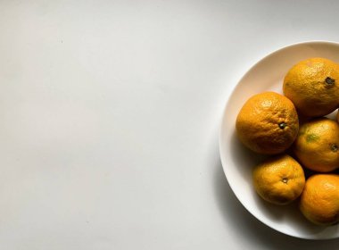 Doğal ışıkta, düz bir yüzeyde, beyaz bir kasede taze toplanmış portakallar.