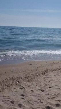 Sahilde güneşli bir günde sakin dalgalar kumsala vuruyor.