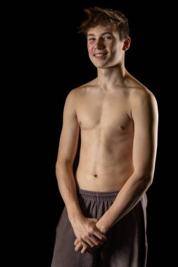 A portrait of a 17 year old shirtless muscular teenage boy against  a black background