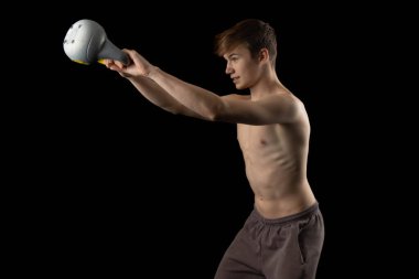 A 17 year old shirtless muscular teenage boy doing kettlebell swings