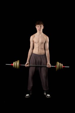 A 17 year old shirtless muscular teenage boy lifting a barbell against a black background
