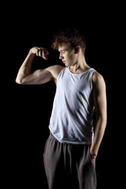 A 17 year old teenage boy wearing a white tank top flexing his arm muscles