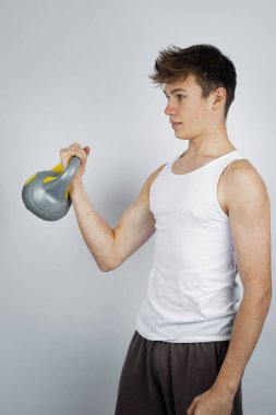 A 17 year old teenage boy wearing a white tank top lifting a kettlebell