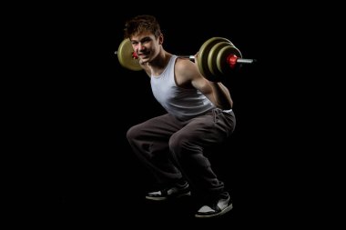 A 17 year old teenage boy wearing a white tank top excercising with a barbell