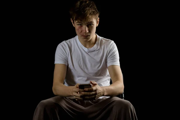 A sitting bored 17 year old teen boy playing with a phone