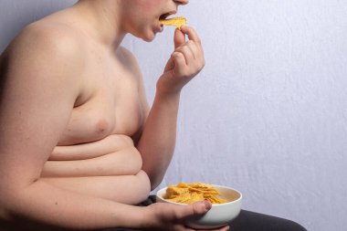 An overweight caucasian teenage boy eating a bowl of crisps clipart