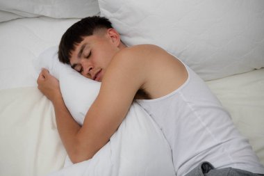 Genç, bekar bir erkek. Kıyafetleriyle, yatağının üstünde uyuyor.