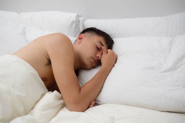 Genç, bekar bir erkek, yatağında, gömleksiz bir şekilde uyuyor.