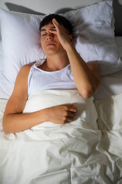 Young single adult man rubbing his eyes as he wakes