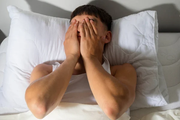 Young single adult man rubbing his eyes as he wakes