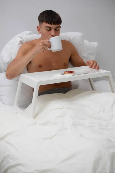 Young single shirtless man having breakfast in bed