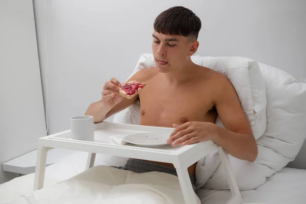 Young single shirtless man having breakfast in bed