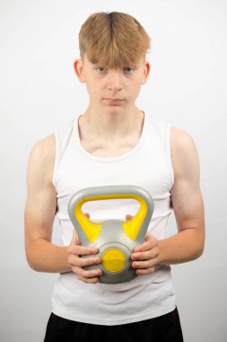 14 yaşında kolsuz yelek giyen beyaz bir gencin portresi. Elinde kettlebell var.