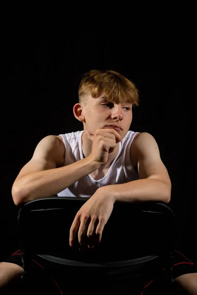 黒い背景の少年に対して椅子に座っている袖のないベストを身に着けている14歳の白人十代の少年肖像画 — ストック写真