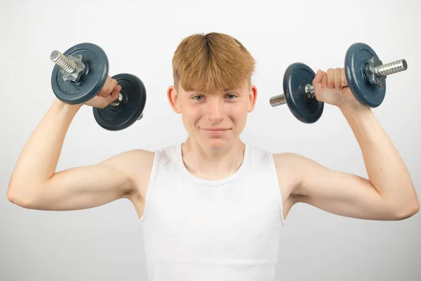 14歳の白人十代の少年が両腕にダンベルを持ち上げる袖口を身に着けている肖像画 — ストック写真
