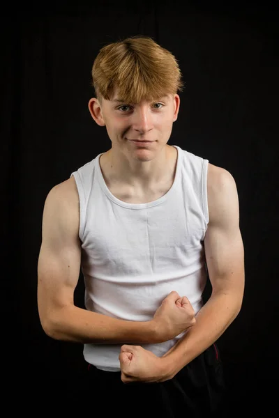 14歳の白人十代の男の子の肖像画は 黒い背景の少年に対して筋肉を柔らかくする袖口を身に着けている — ストック写真