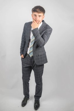 Takım elbiseli ve kravatlı genç bir girişimcinin portresi sade bir arka plana doğru eğiliyor.