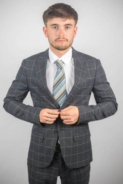 Takım elbiseli ve kravatlı genç bir girişimcinin portresi düz bir arkaplanda ceketini düzeltiyor.