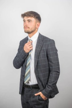 Takım elbiseli genç bir girişimcinin portresi kravatını düz bir arkaplana göre ayarlıyor.