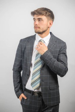 Takım elbiseli genç bir girişimcinin portresi kravatını düz bir arkaplana göre ayarlıyor.