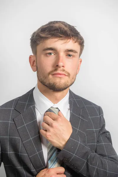 若い起業家の肖像画は 明白な背景に対して彼のネクタイを調整するスーツで — ストック写真