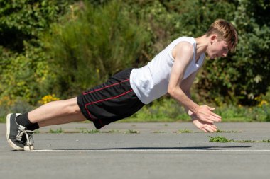 Formda ve sportif genç bir çocuk sıcak bir yaz gününde dışarıda şınav çekiyor.