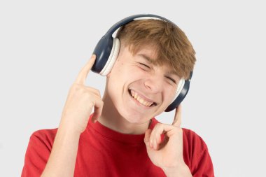 Mutlu ve gülümseyen 15 yaşında genç bir çocuk, kırmızı tişört giyiyor, kulaklıkla müzik dinliyor. 