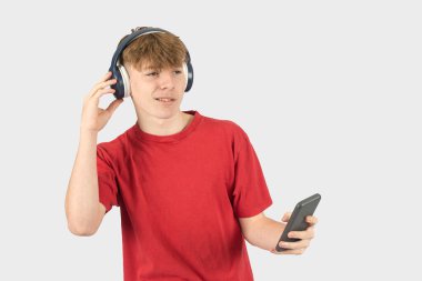 Telefonuyla müzik dinleyen on beş yaşında gülümseyen bir gencin stüdyo portresi.