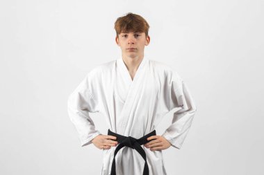 15 yaşında, karate takımından, elleri kalçasında A Gi giyen bir çocuk.