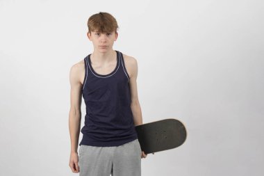 15 yaşında kaykaycı bir çocuk beyaz bir arka plana karşı kaykay tutuyor.