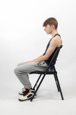 15 yaşında kolsuz bir bluz ve eşofmanlı bir çocuk yan koltukta oturuyor.