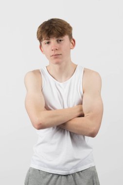 15 yaşında genç bir çocuk beyaz bir arka plana karşı duruyor ve çapraz kollarla ileriye bakıyor.