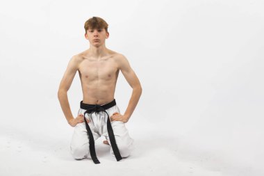 15 yaşında, üstsüz, siyah kemerli, Gi pantolonlu, diz çökmüş bir çocuk.