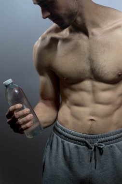 Karın kasları ve göğsü iyi tanımlanmış genç bir erkek cesedi. Gömleksiz gövdesi olan bir şişe su tutan manken. Vücut bakımı, erkek sağlığı, fitness, gençlik, erkeklik, sağlık, kilo kaybı, vücut geliştirme 
