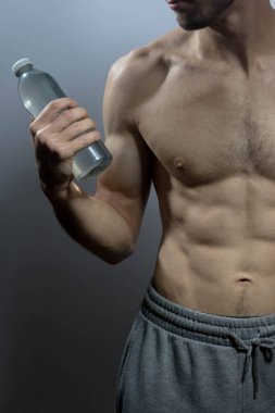 Karın kasları ve göğsü iyi tanımlanmış genç bir erkek cesedi. Gömleksiz gövdesi olan bir şişe su tutan manken. Vücut bakımı, erkek sağlığı, fitness, gençlik, erkeklik, sağlık, kilo kaybı, vücut geliştirme 