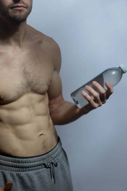 Karın kasları ve göğsü iyi tanımlanmış genç bir erkek cesedi. Gömleksiz gövdesi olan bir şişe su tutan manken. Vücut bakımı, erkek sağlığı, fitness, gençlik, erkeklik, sağlık, kilo kaybı, vücut geliştirme 