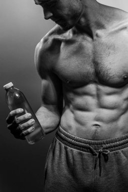 Su şişesi tutan genç bir erkek cesedi. Kasları ve göğsü iyi tanımlanmış. Gömleksiz gövdeli bir model. Vücut bakımı, erkek sağlığı, fitness, gençlik, erkeklik, sağlık, kilo kaybı, vücut geliştirme 