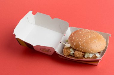 London, United Kingdom, 12th November 2024:- A view of a McDonalds Vegetable Deluxe Burger, against a Red background clipart