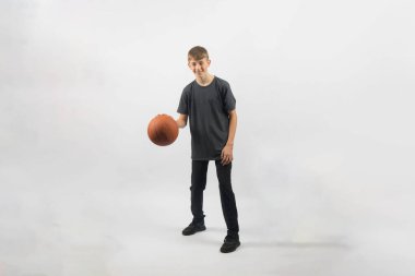 15 yaşında genç bir çocuk basketbol topunu sektiriyor. Stüdyoda beyaz bir arka plana karşı çekim yapıyor.