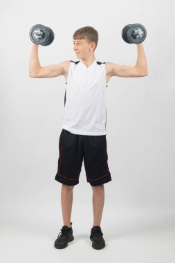 Fifteen year old teenage boy exercising with dumbbells, studio shot against a white background clipart