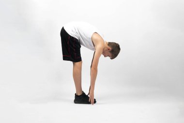 15 yaşında genç bir çocuk ayak parmaklarına dokunuyor. Stüdyoda beyaz bir arkaplana karşı çekim yapıyor.