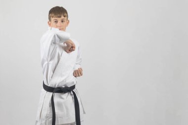 On beş yaşındaki genç erkek karate siyah kuşağı beyaz bir arkaplana karşı atölye çekimlerinde dirsek darbesi yapıyor.