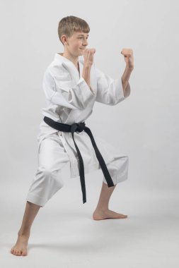 15 yaşında, erkek, karate siyah kuşağı. Duruşu düşük. Stüdyo, beyaz bir arka plana karşı.