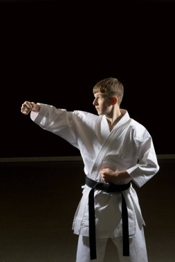 Fifteen year old male teenage karate black belt doing a side back fist, studio shot against a black background clipart