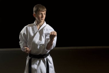 Fifteen year old male teenage karate black belt doing a body block, studio shot against a black background clipart