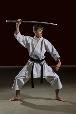 On beş yaşında, erkek, karate siyah kuşağı var. Kılıç kullanıyor. Stüdyoda, siyah arka planda.