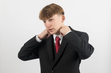 Yakasını düzelten takım elbiseli 16 yaşındaki genç bir çocuk, beyaz bir arka planda çekim yapıyor.