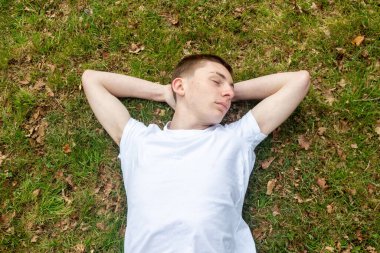 Genç bir çocuk bahar günü çimenlerde kestiriyor.