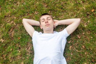 Genç bir çocuk bahar günü çimenlerde kestiriyor.